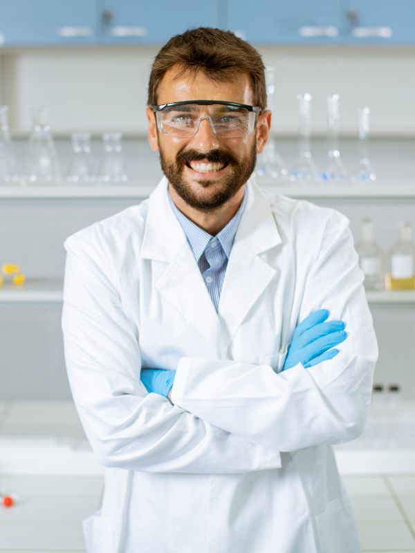 bearded man wearing lab coat and safety goggles in a Cosmetics Industry Training facility.